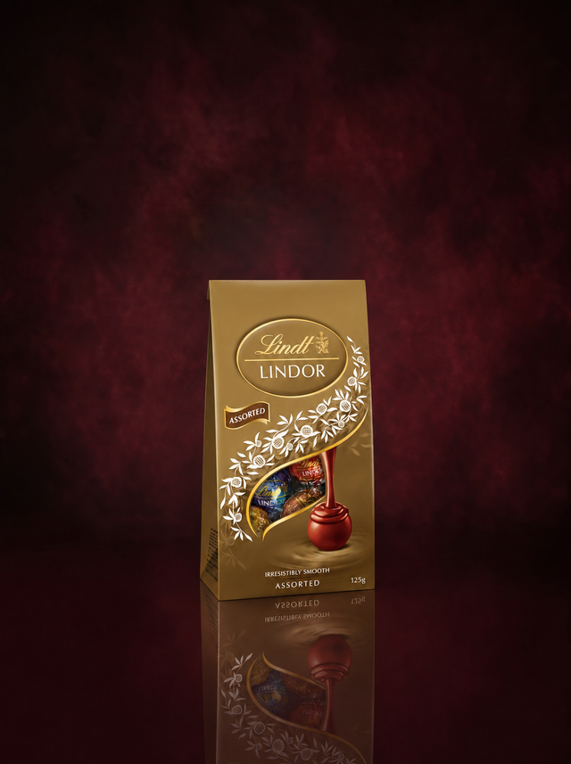 A gold 125g bag of Lindt Lindor Assorted truffles standing on a dark reflective surface