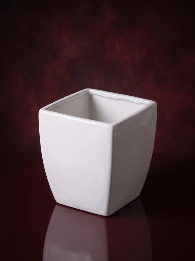 A white glazed ceramic vase, square with softly tapered sides, empty on a dark reflective surface