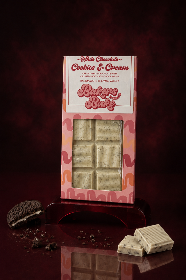 Bakers Wanna Bake white chocolate Cookies and Cream block in its pink window carton, a chocolate cookie and a broken square beside it