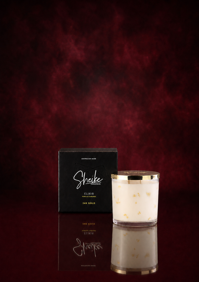 Sheike Elixir 24K gold candle in Vanilla Caramel, cream wax flecked with gold leaf beside its black gift box